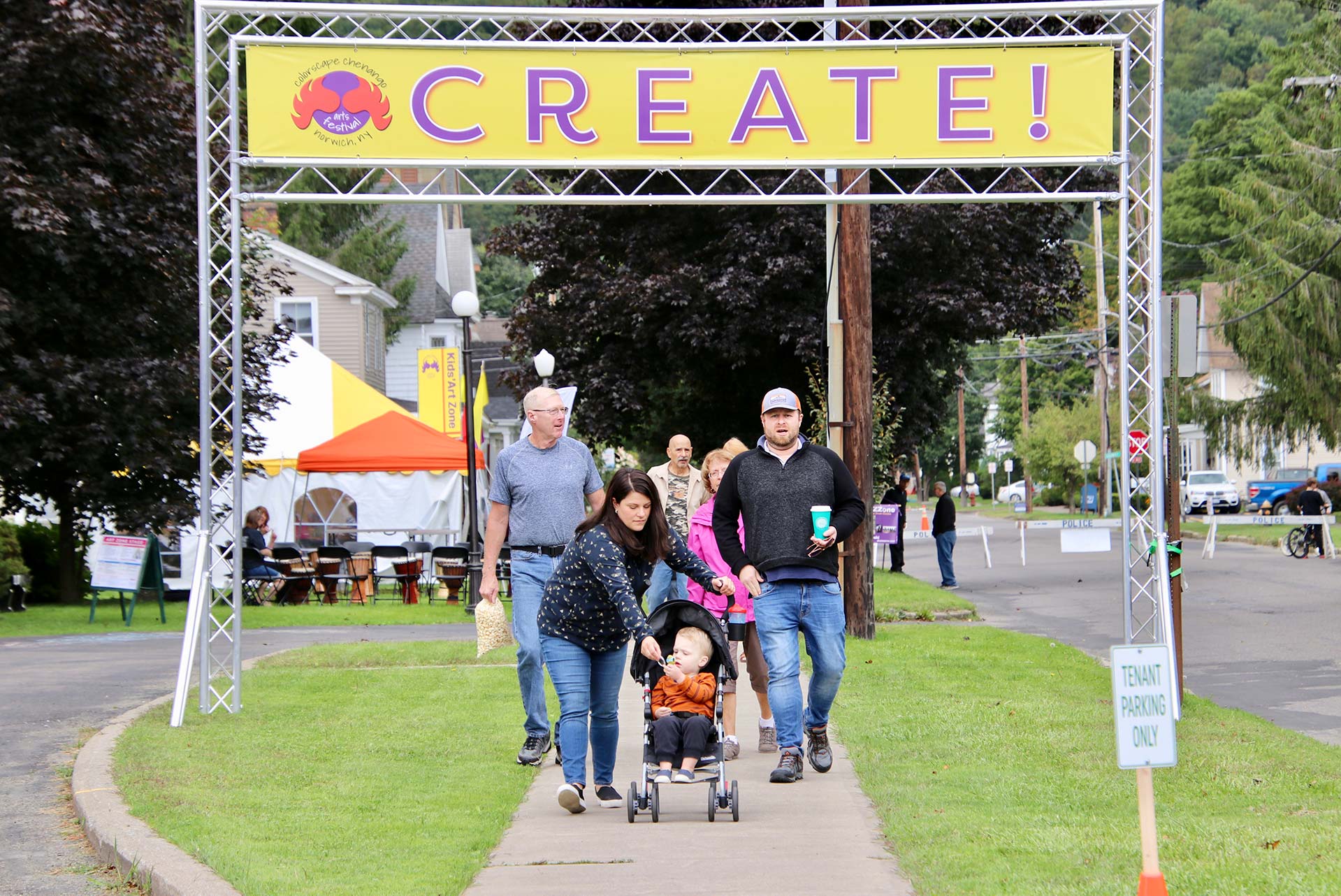 A family with young children walks under a large banner that says CREATE! at the Colorscape Chenango Arts Festival