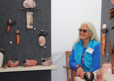 An artist smiles in her booth showing vases and sculptures at the Colorscape Chenango Arts Festival
