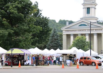A distant view of the Colorscape Chenango Arts Festival shows many artist booths in the lawn in front of the Chenango County Court House